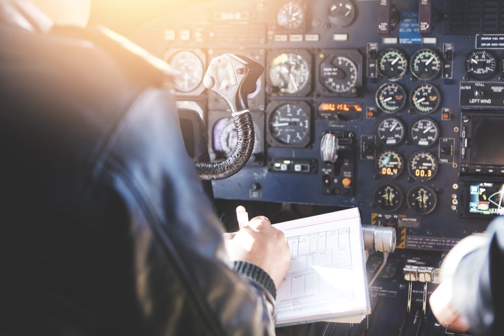 Rear view of pilots in a jet airliner cockpit, one holding a pen and writing on preflight paperwork
